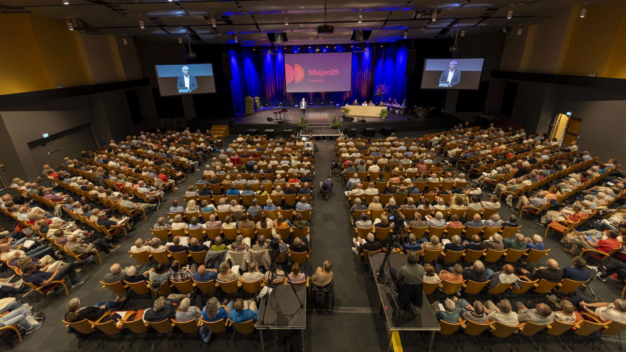 Oversiktsbilde over fullsatt sal med generalsekretær på scenen