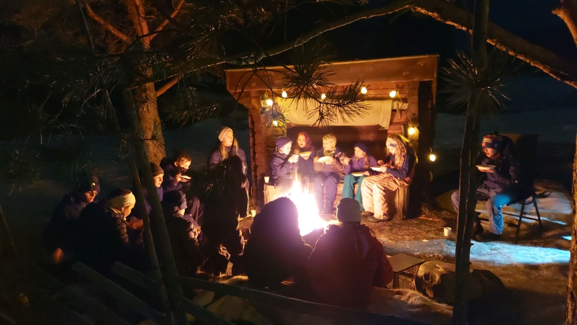 En gruppe barn og voksne rundt leirbål ved gapahuk
