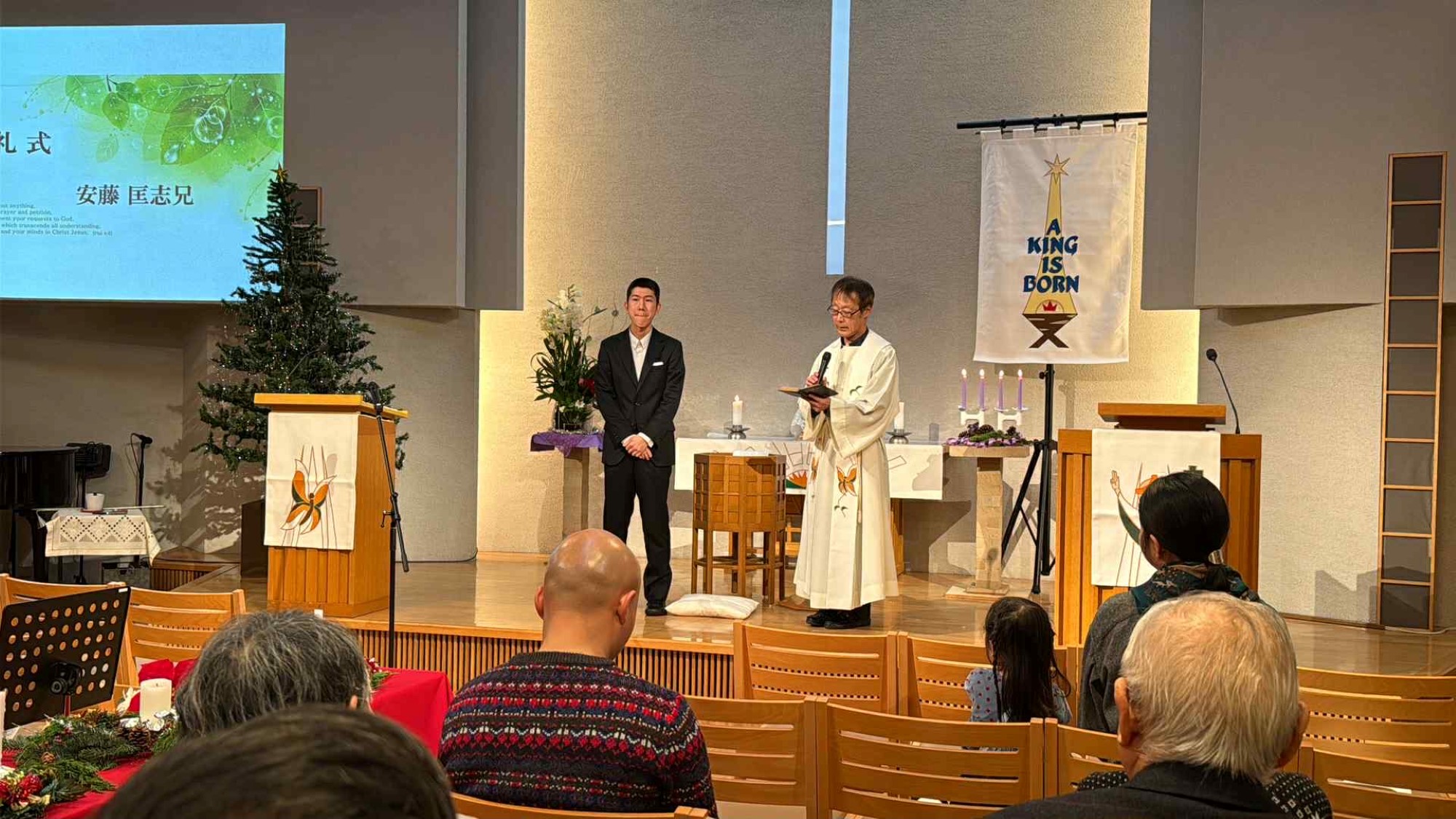 En ung mann står foran forsamlingen og bekjenner at han vil følge Jesus. Presten står ved siden av ham.