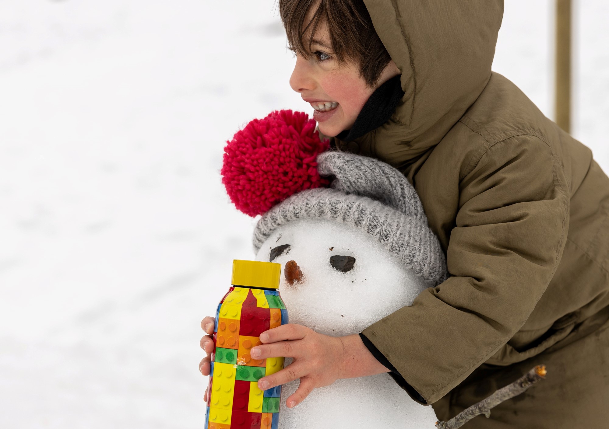 Gutt som holder rundt en snømann med en flaske med legomotiv i hånden