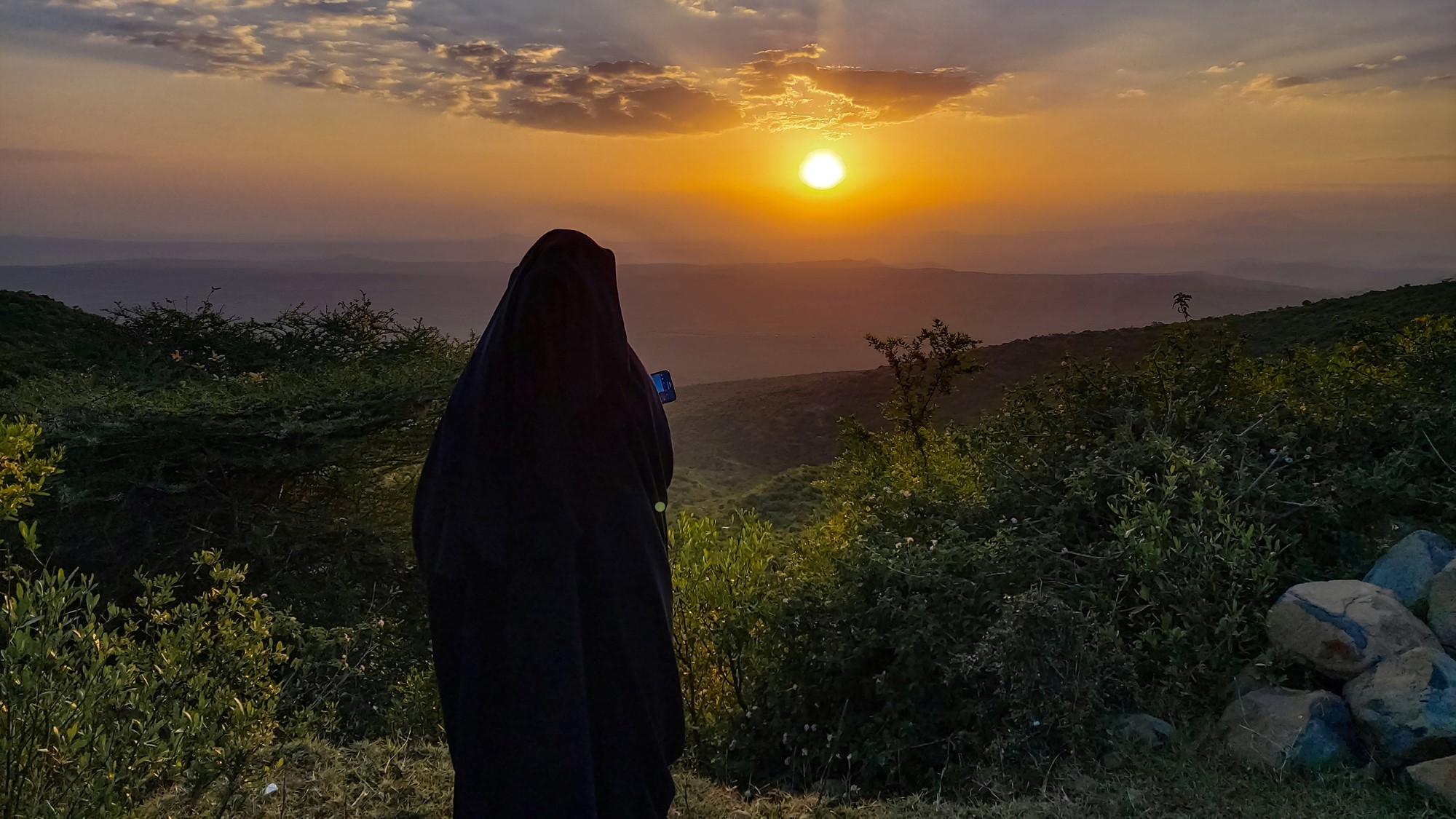 Tildekket kvinne ser utover landskap i solnedgang