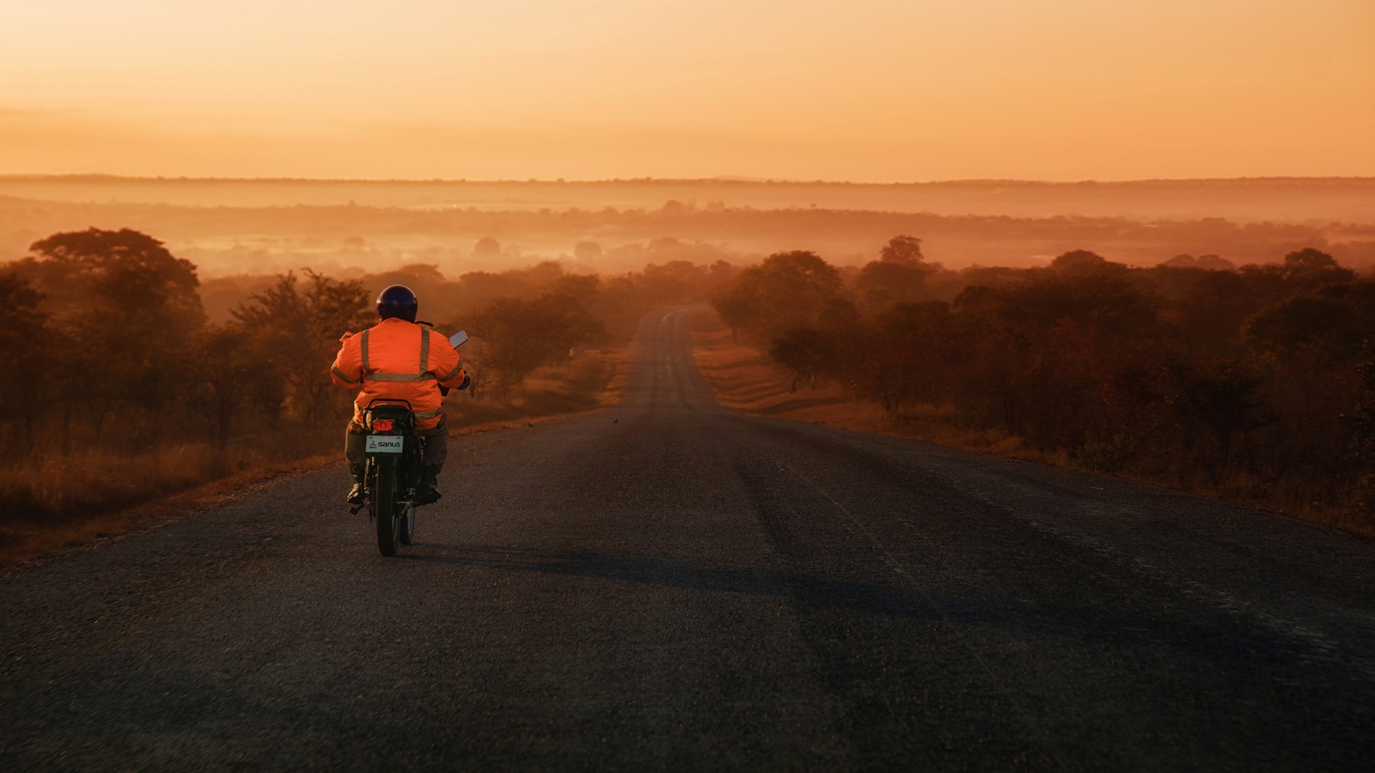 Mann på motorsykkel i åpent afrikansk landskap i solnedgang