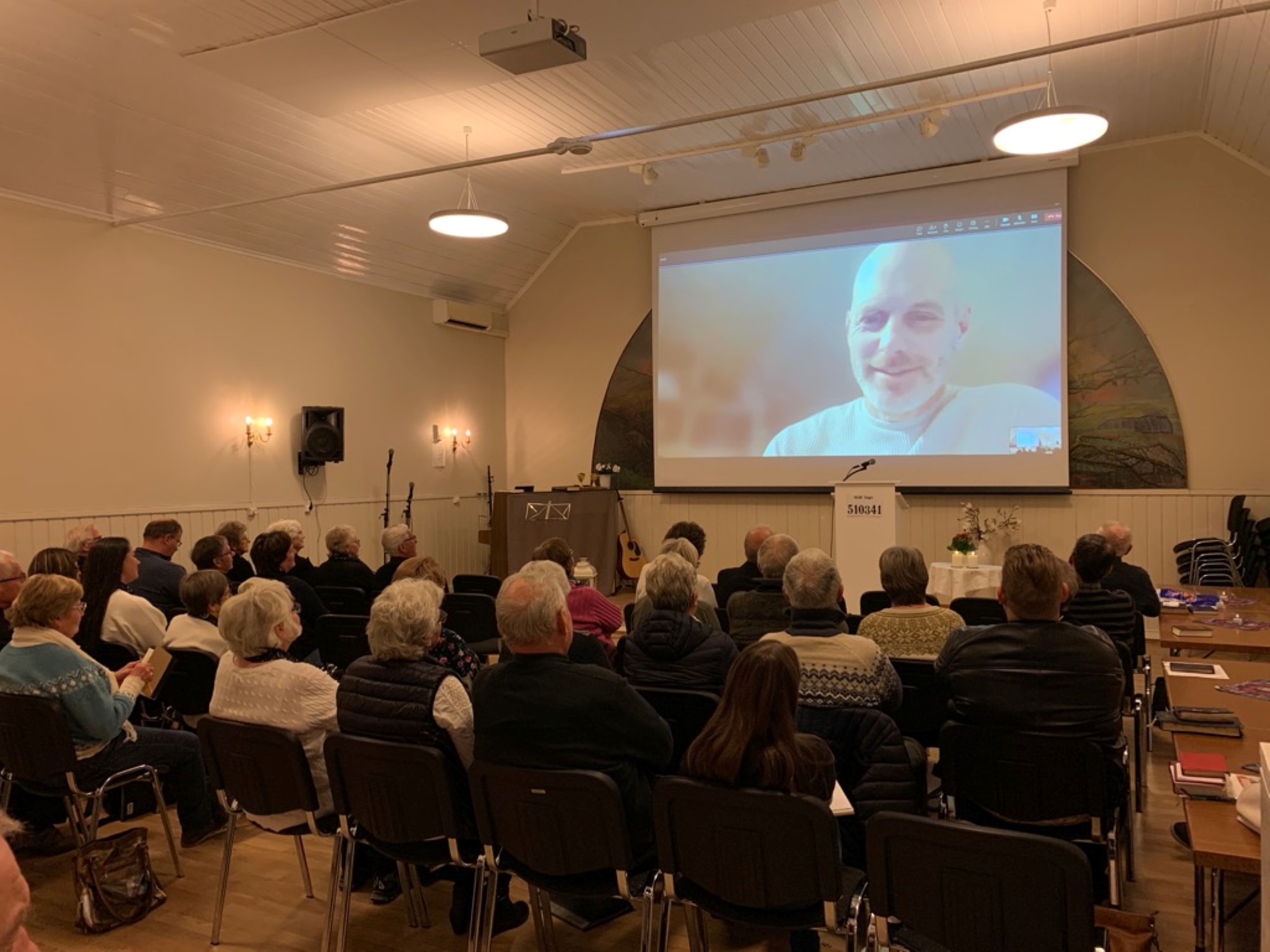 Forsamling og talar på skjerm