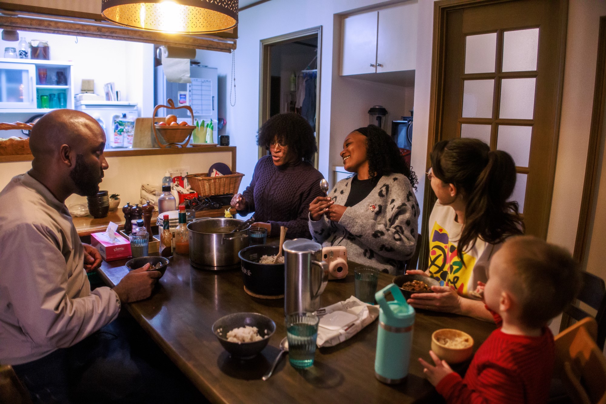 Internasjonalt fellesskap rundt middagsbordet. Fire unge voksne og et barn.