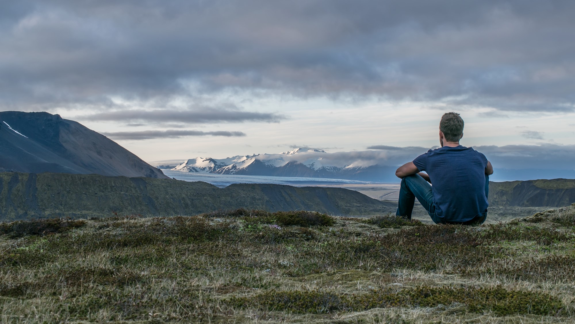 Mann sitter på fjellvidde og ser utover majestetisk landskap med fjell og fjord