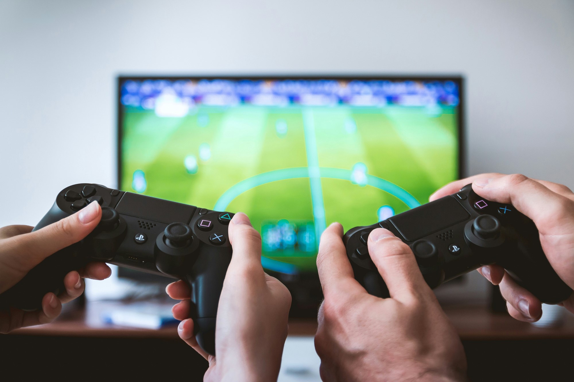 To par hender holder hver sin spillkonsoll, med FIFA-spill i bakgrunnen