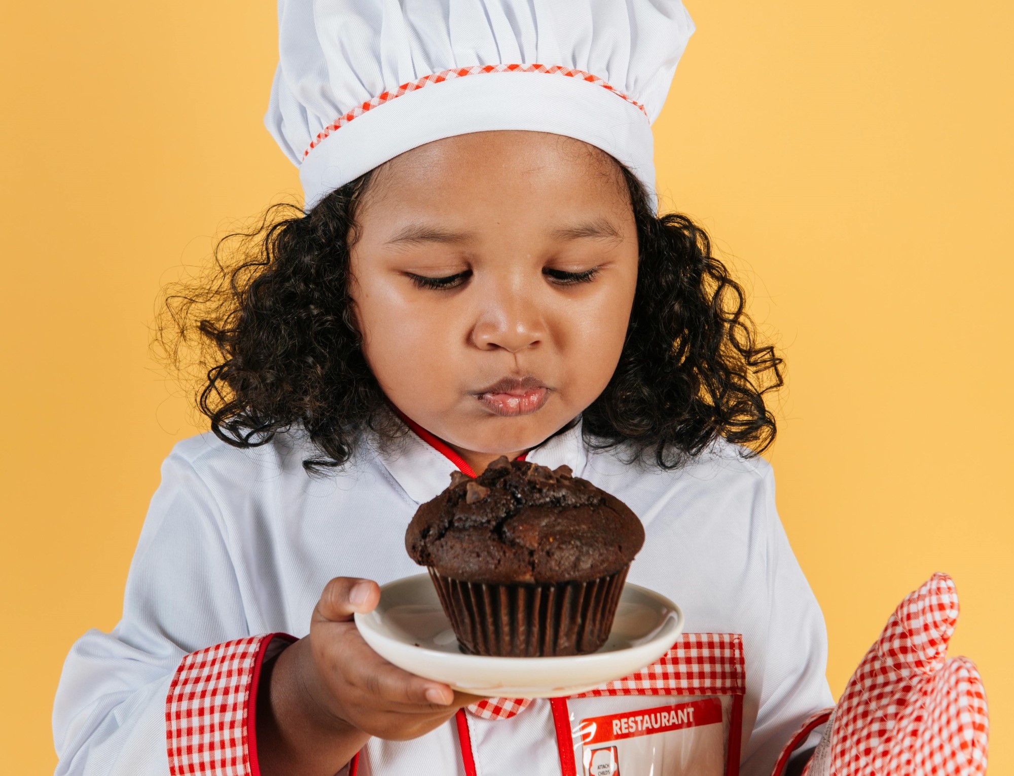 Liten jente i kokkeklær holder muffin