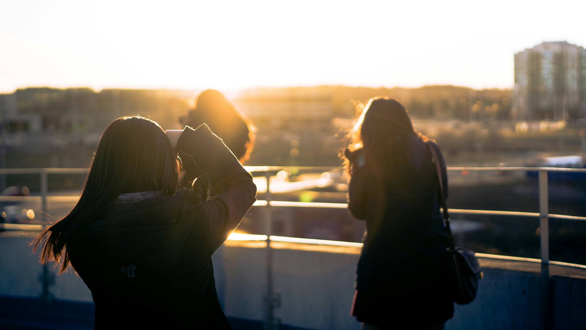 To unge kvinner tar bilder av solnedgangen i by