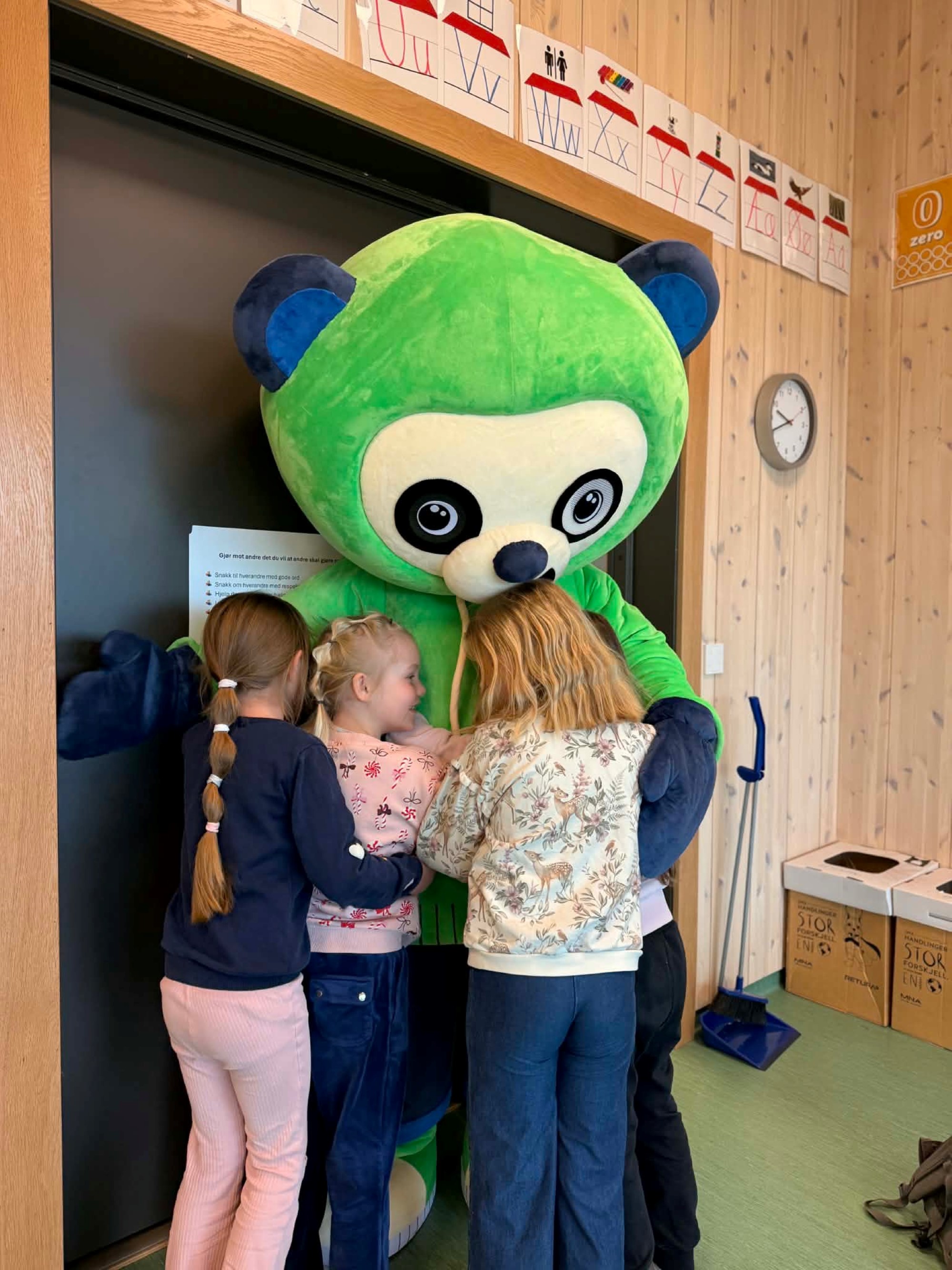 Stor, grønn maskot får klemmer av tre jenter