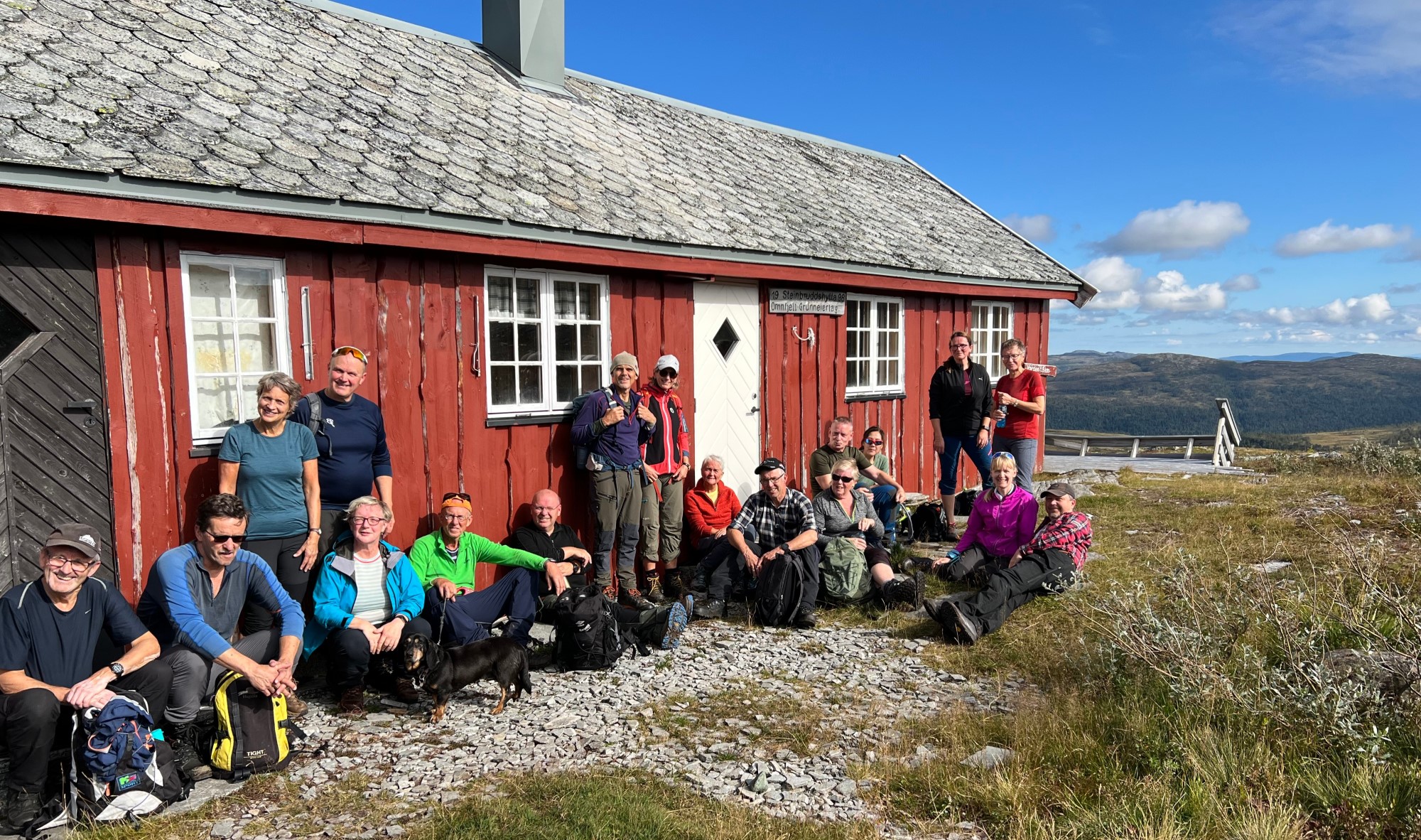 Glade mennesker i solveggen utenfor fjellhytte