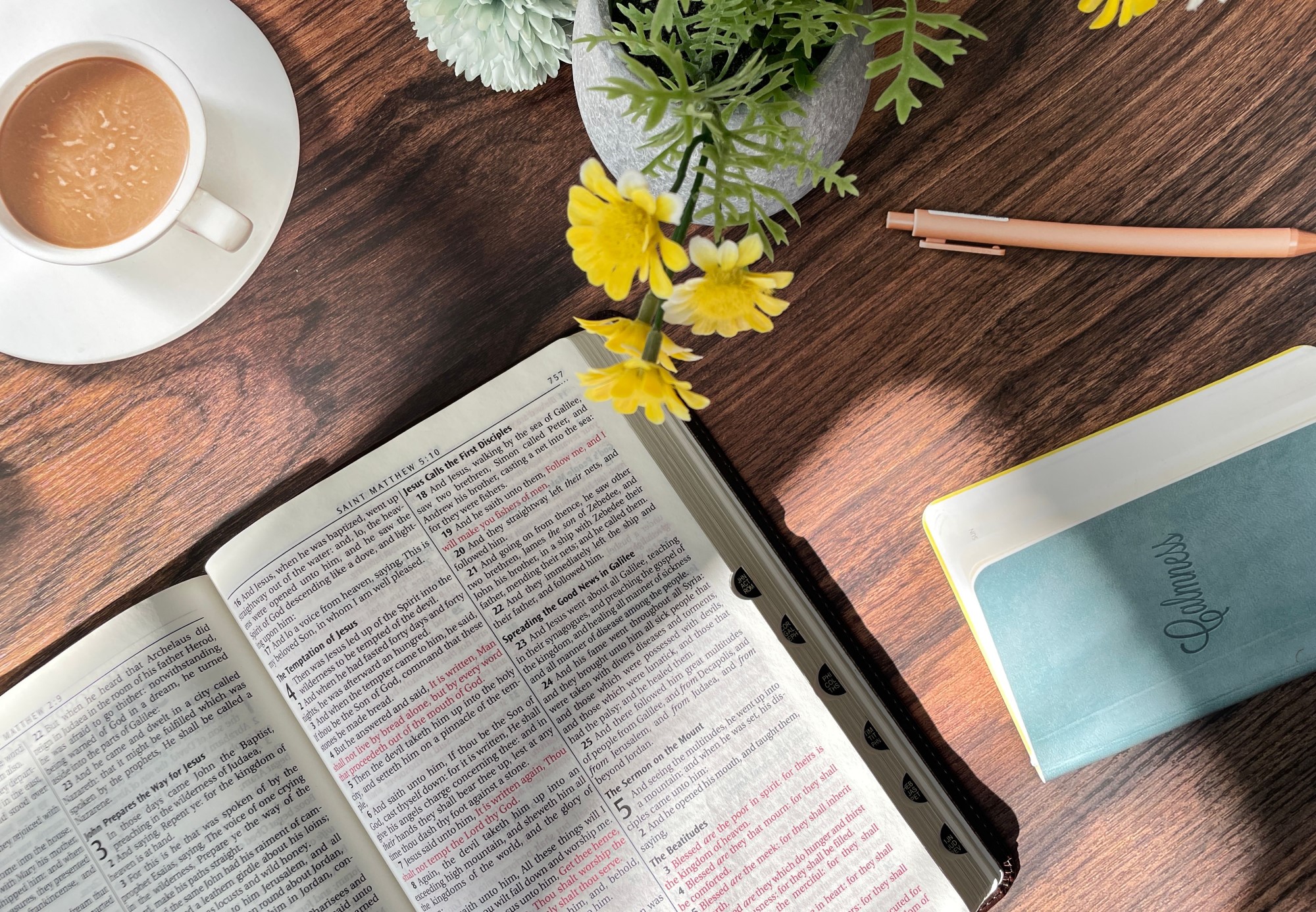 Oppslått bibel på bord, med kaffekopp og blomster
