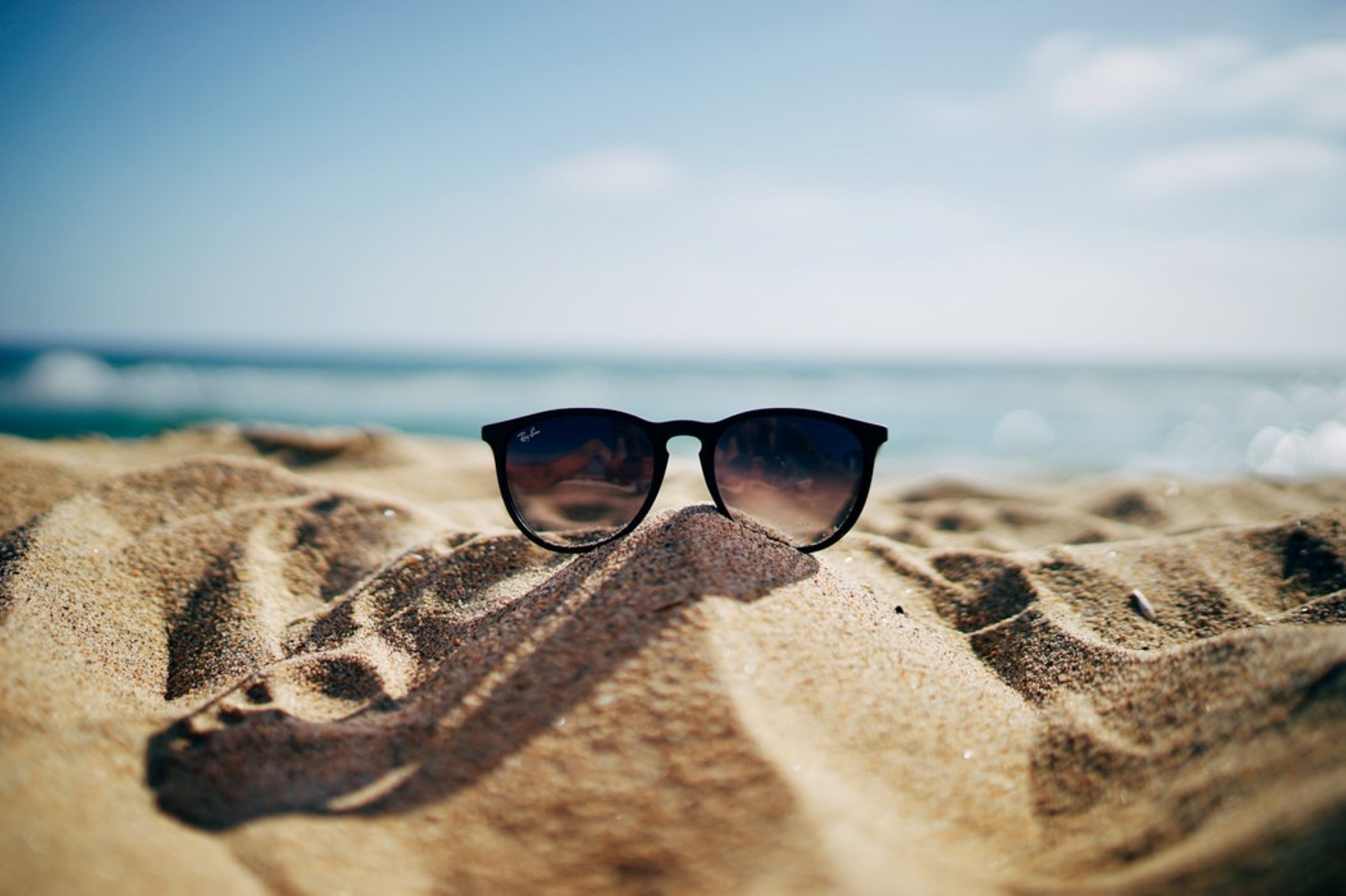 Solbriller i sand foran sjø