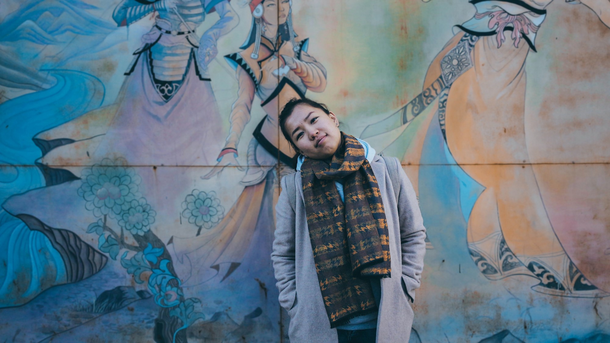 Ung mongolsk kvinne foran murvegg med veggmaleri
