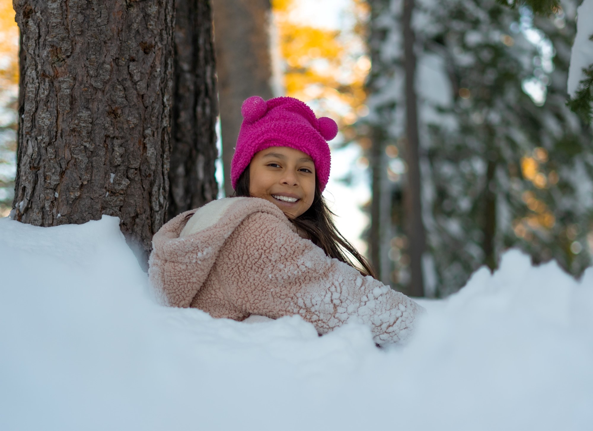 Jente som sitter i snøen i skogen