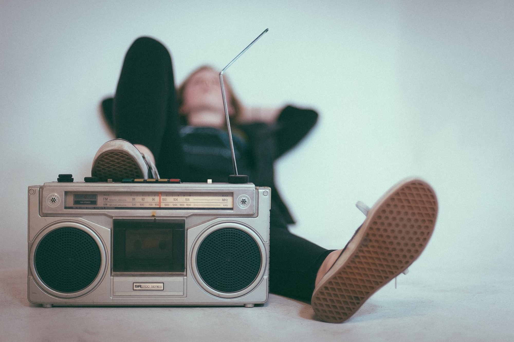 Bildet viser en gammeldags radio og en person som ligger i bakgrunne og hører på radio