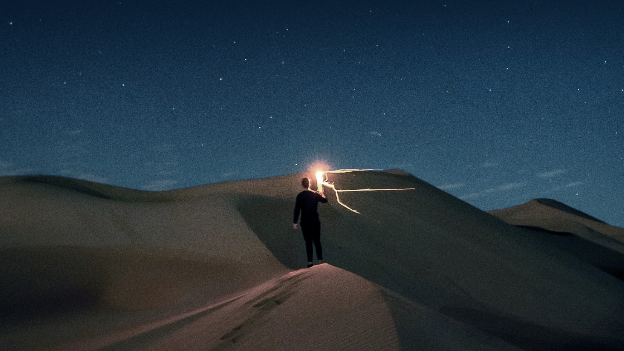 Mann holder lys mot stjernehimmel i ørken